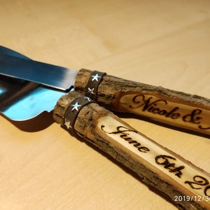 May include: A set of two wooden cake cutting knives with leather wraps and engraved text. The top knife reads "Nicole & Jason" and the bottom knife reads "June 6th 2021".