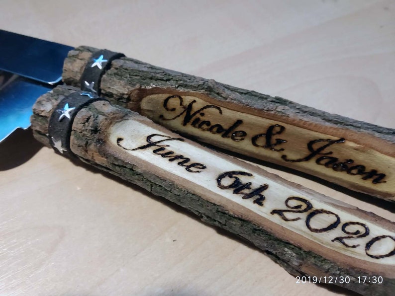 May include: A pair of wooden cake cutting knives with black leather handles and silver stars. The handles are engraved with "Nicole & Jason" and "June 6th 2020".