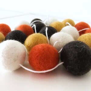 May include: A garland of felt balls in orange, white, black, and yellow. The balls are strung together with white thread.