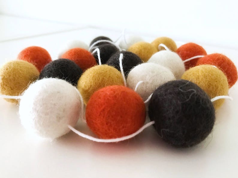 May include: A garland of felt balls in orange, white, black, and yellow. The balls are strung together with white thread.