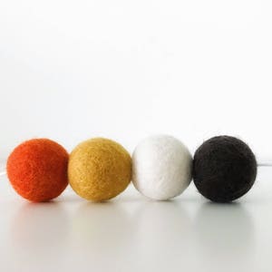 May include: A garland of four felt balls in orange, yellow, white, and black colors. The balls are strung together with white thread.