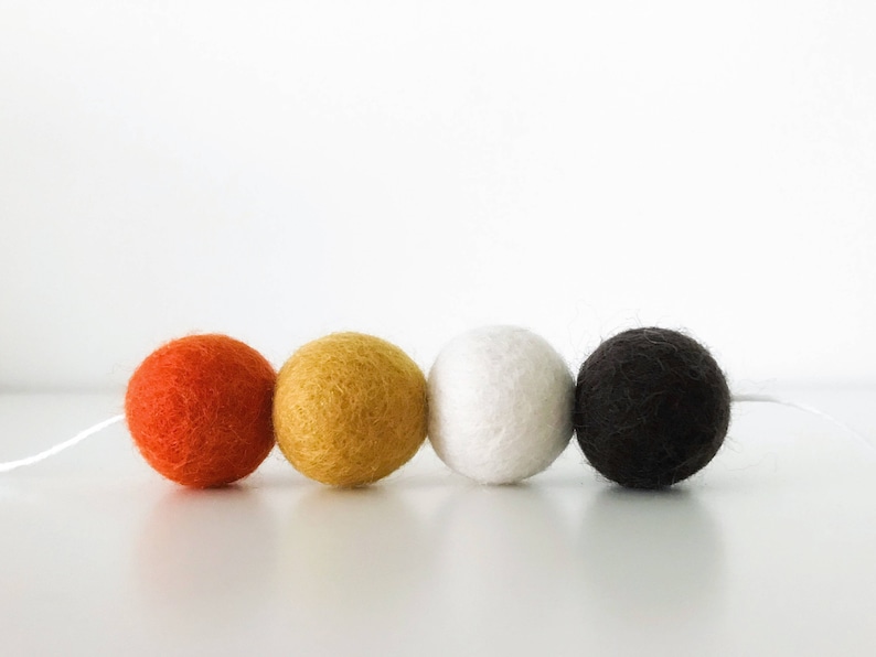 May include: A garland of four felt balls in orange, yellow, white, and black colors. The balls are strung together with white thread.
