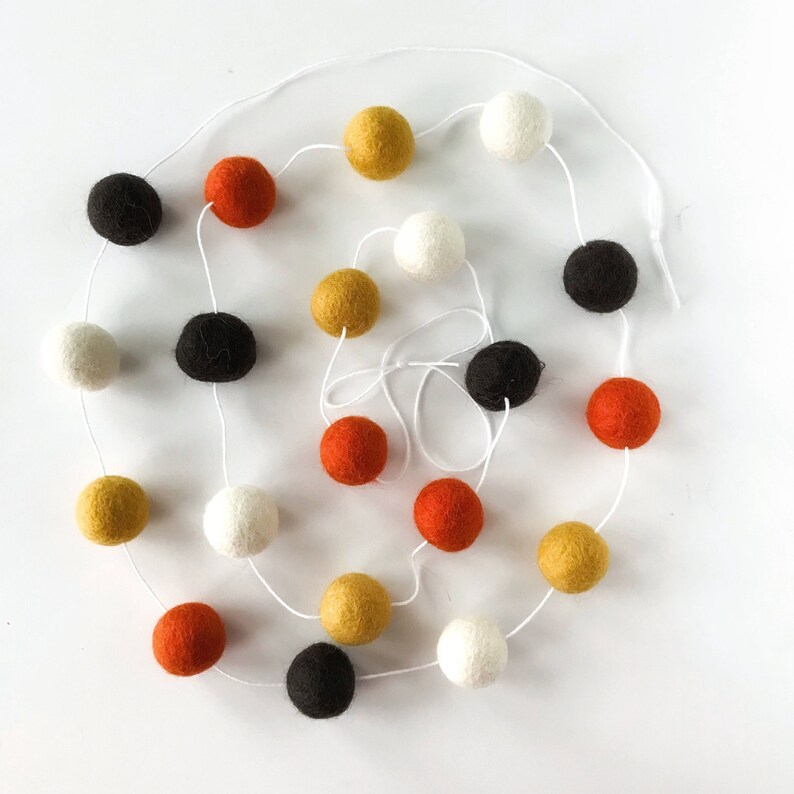 May include: A garland of felt balls in black, white, orange, and gold colors. The balls are strung on a white string.