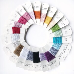 May include: A collection of 16 spools of colorful twine, each with a white label that reads "Gracie & Marie". The twine is arranged in a circle, with the labels facing outward.