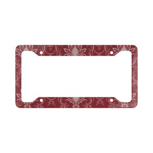 May include: A rectangular license plate frame with a burgundy background and a repeating floral pattern in cream and white. The frame has four mounting holes and a smooth, glossy finish.