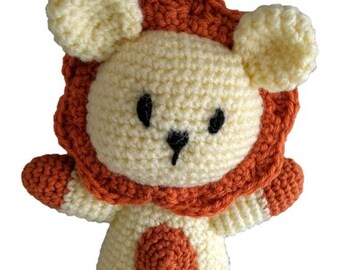 Puede incluir: Un león de peluche tejido a crochet con un cuerpo de color crema y una melena, patas y una mancha en el vientre de color naranja.