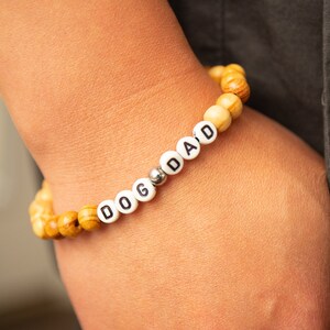 May include: A wooden bead bracelet with the word "DOG DAD" spelled out in white beads.