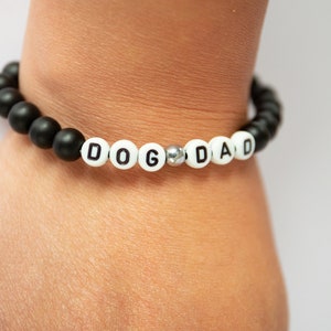 May include: A black and white beaded bracelet with the word "DOG DAD" spelled out in white beads.