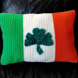May include: A green, white and orange crocheted cushion with a shamrock design in the centre.