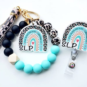 May include: A turquoise and black beaded bracelet with a gold charm and a keychain with a turquoise and black leopard print rainbow charm with the text "Let all you do be done in love 1 Corinthians 16:14" and "SLP".