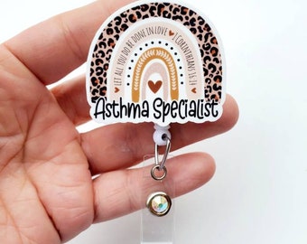 Op de afbeelding: Een badge reel met een regenboogontwerp en de woorden "Asthma Specialist". De regenboog heeft een luipaardprintpatroon en inspirerende tekst. De reel heeft een doorzichtige plastic clip en een decoratieve edelsteen.