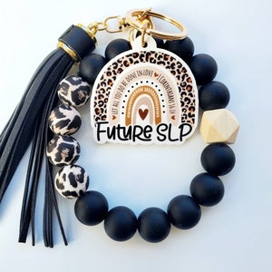 May include: Black and leopard print beaded bracelet with a gold key chain and a charm that says "Future SLP" with a rainbow and the text "Let all you do be done in love 1 Corinthians 16:14".