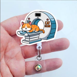 May include: A badge reel featuring a cartoon cat undergoing a CAT SCAN. The cat is orange and white, lying on a blue and white examination table. The CAT SCAN machine is white and blue, with the words "CAT SCAN" in orange.