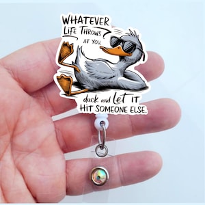 May include: A white retractable badge holder with a cartoon duck wearing sunglasses and the text "WHATEVER LIFE THROWS AT YOU, duck and let it HIT SOMEONE ELSE."