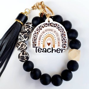 May include: Black and leopard print beaded keychain with a gold key ring and a white charm with a rainbow and the text "Making a big difference in little lives Teacher".