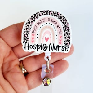 May include: White badge reel with a pink and black leopard print rainbow design. The rainbow has a pink and white background with a gold outline. The text on the badge reel reads "Because your life is worth my time." and "Hospice Nurse".