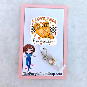 May include: A pink card with the text "I love Fall (Prevention)" and a cartoon image of two orange socks with faces. A cartoon image of a woman in a blue scrub top is in the lower left corner. A clear badge holder with a silver clip and a sparkly rhinestone is attached to the card.