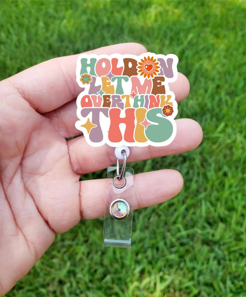 May include: A colorful badge holder with the text "Hold on let me overthink this" in a retro font. The badge holder has a clear plastic strap and a sparkly rhinestone.