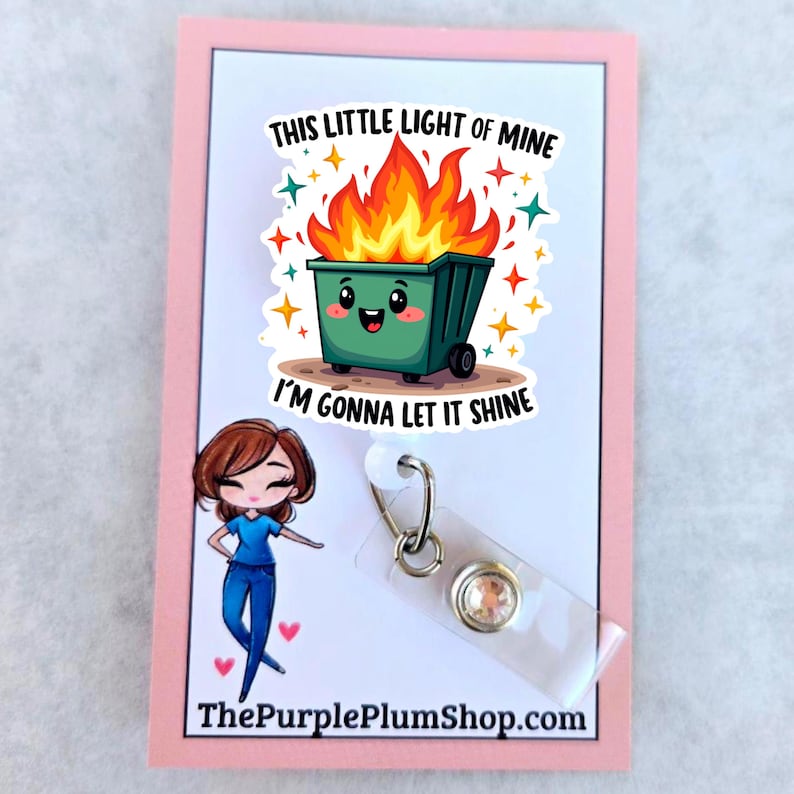 Op de afbeelding: Een groene cartoon vuilnisbak met een glimlachend gezicht staat in brand met de tekst "This little light of mine I'm gonna let it shine". De afbeelding staat op een witte kaart met een roze rand. Een doorzichtige badgehouder met een strasssteen is aan de kaart bevestigd.