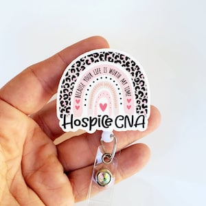 May include: A pink and black leopard print rainbow with the text "Because your life is worth my time" and "Hospice CNA". The rainbow has a white background and is attached to a clear retractable badge holder with a silver clip and a clear jewel.