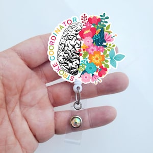 May include: White badge reel with a colorful floral design and a black and white brain illustration. The text "STROKE COORDINATOR" is written around the edge of the reel.