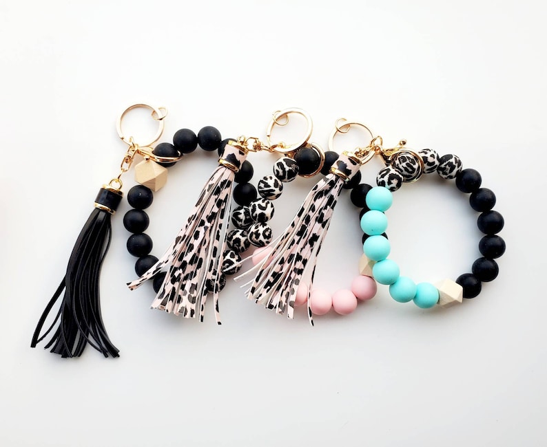 May include: Three beaded keychains with tassels. One keychain has black beads, one has black and white leopard print beads, and one has pink and turquoise beads.