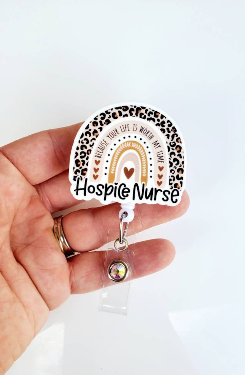 May include: A white and brown leopard print rainbow with the text "Because your life is worth my time" and "Hospice Nurse". The rainbow has a heart in the center and is attached to a clear retractable badge holder with a sparkly rhinestone.