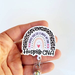 May include: A white and black leopard print rainbow with the text "Because your life is worth my time" and three pink hearts. The rainbow is attached to a white retractable badge holder with a clear plastic strap and a silver clip. The text "Hospice CNA" is printed below the rainbow.