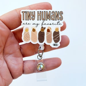 May include: White badge reel with a white background and the text "Tiny Humans are my favorite -NICU-" in black. There are five illustrations of swaddled babies in different skin tones.