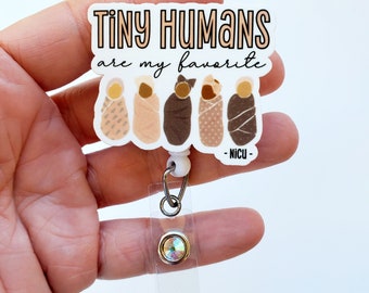 May include: White badge reel with a white background and the text "Tiny Humans are my favorite -NICU-" in black. There are five illustrations of swaddled babies in different skin tones.
