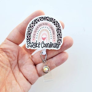 May include: A white badge holder with a pink and black leopard print rainbow design. The rainbow has the text "Let all you do be done in love 1 Corinthians 16:14" and the text "Stroke Coordinator". The badge holder has a clear retractable badge reel with a sparkly crystal.