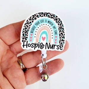 May include: A white and blue rainbow with a leopard print border and the text "Because your life is worth my time" and "Hospice Nurse". The rainbow has a pink and peach center and pink hearts. The badge holder has a clear plastic strap and a clear plastic badge holder with a sparkly gem.