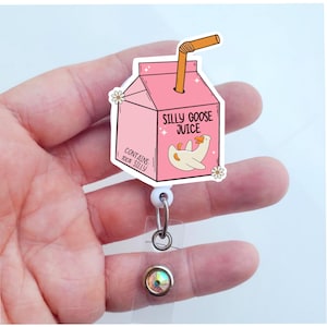 May include: Pink and white cartoon goose juice box with a straw, a white retractable badge reel, and a clear crystal charm. The juice box says "Silly Goose Juice" and "Contains 100% Silly".