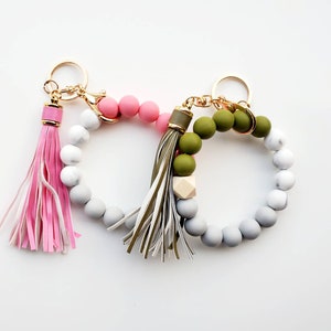 May include: A set of two beaded keychains with tassels. One keychain has pink and white beads with a pink tassel. The other keychain has green and white beads with a green and white tassel.