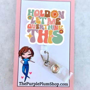 May include: A white plastic badge holder with a colorful retro-style sticker that says "Hold on let me overthink this". The sticker has flowers and hearts. A cartoon illustration of a woman in blue scrubs is on the left side of the holder. The holder has a clear plastic badge holder with a sparkly rhinestone.