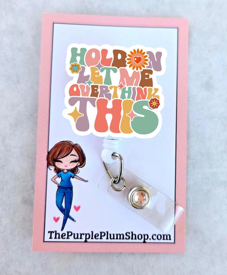 May include: A white plastic badge holder with a colorful retro-style sticker that says "Hold on let me overthink this". The sticker has flowers and hearts. A cartoon illustration of a woman in blue scrubs is on the left side of the holder. The holder has a clear plastic badge holder with a sparkly rhinestone.