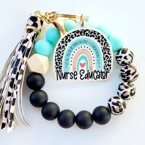 May include: A keychain wristlet with a "Nurse Educator" charm. The charm features a rainbow design with leopard print accents and the text "Let all you do be done in love". The wristlet includes black, turquoise, and leopard print beads, and a tassel.