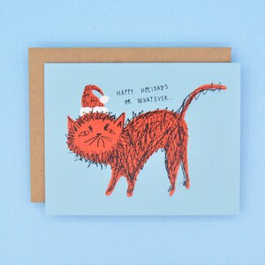 May include: A blue greeting card with a red cat wearing a Santa hat. The text on the card reads "Happy Holidays or Whatever..."