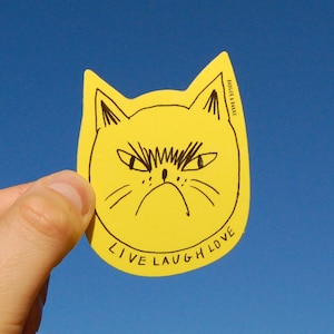 May include: Yellow sticker with a black line drawing of a cat with an angry expression. The sticker says "Live Laugh Love" and "Rodger & Burke" in the upper right corner.