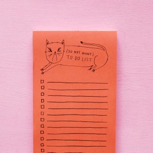 May include: Orange notepad with a black line drawing of a cat with the text "(Do Not Want) To Do List" at the top. The notepad has 15 lines for writing.