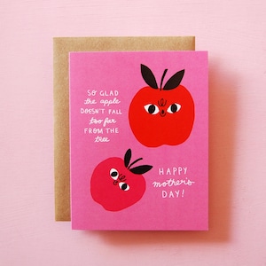 May include: A pink Mother's Day card featuring two cartoon red apples with black stems and leaves. The card has the text "So glad the apple doesn't fall too far from the tree" and "Happy Mother's Day!" in white.