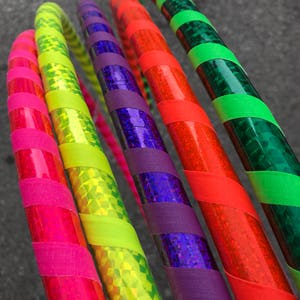 May include: Five colorful hula hoops with iridescent tape. The hoops are arranged in a fan shape, with the green hoop at the top and the pink hoop at the bottom. The hoops are all different colors, including green, red, purple, yellow, and pink.