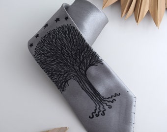 May include: A gray silk tie with a black embroidered tree design. The tree has a thick trunk and branches with small stars at the top.