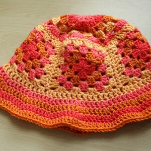 May include: A crocheted sun hat with a wide brim in shades of orange, pink, and peach.