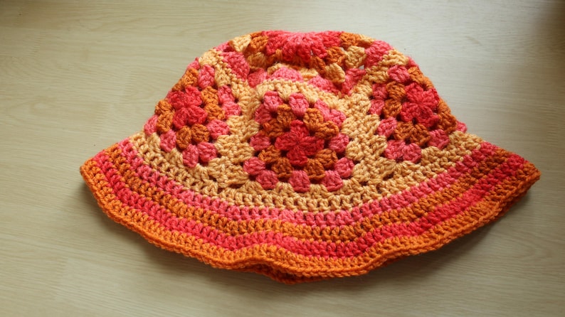 May include: A crocheted sun hat with a wide brim in shades of orange, pink, and peach.