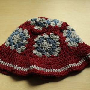 May include: A red crocheted bucket hat with a gray and blue geometric pattern.
