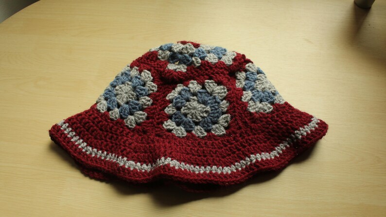 May include: A red crocheted bucket hat with a gray and blue geometric pattern.