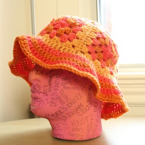 May include: A crocheted sun hat with a wide brim in orange and pink. The hat is on a pink mannequin head.