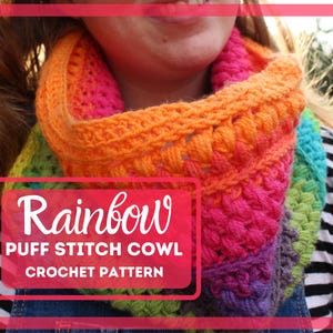 May include: A rainbow crochet cowl with a puff stitch pattern. The cowl is made in a variety of colors, including red, orange, yellow, green, blue, and purple. The cowl is worn by a person with long brown hair.
