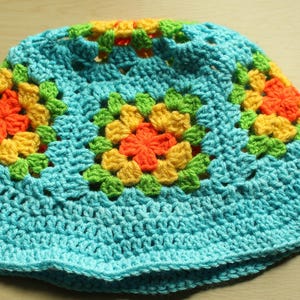May include: A crocheted sun hat with a blue base and colorful squares featuring yellow, orange, and green accents.